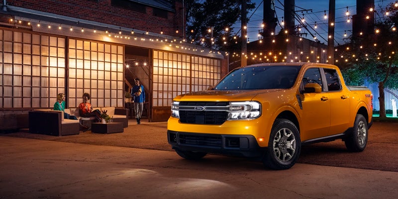 Family and friends having a get together around their brand new yellow 2023 Ford Maverick surrounded by beautiful ambient lighting.