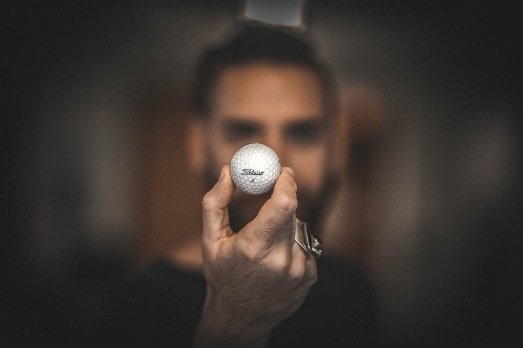 man holding a golf ball in front of his face with his profile blurred with the background.
