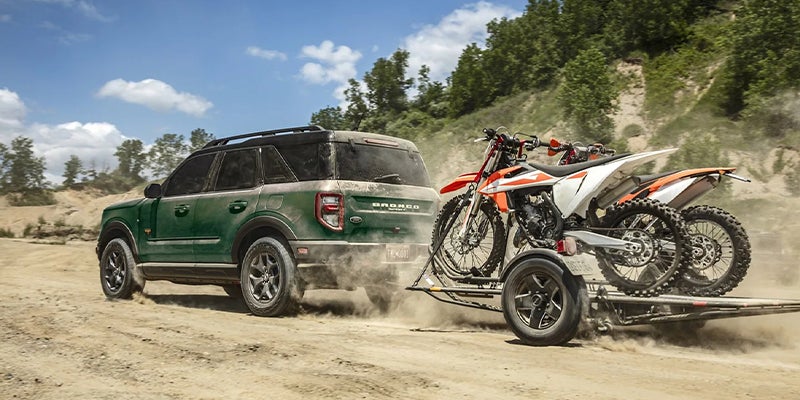 brand new 2023 Ford Bronco hauling dirt bikes on an off road path.